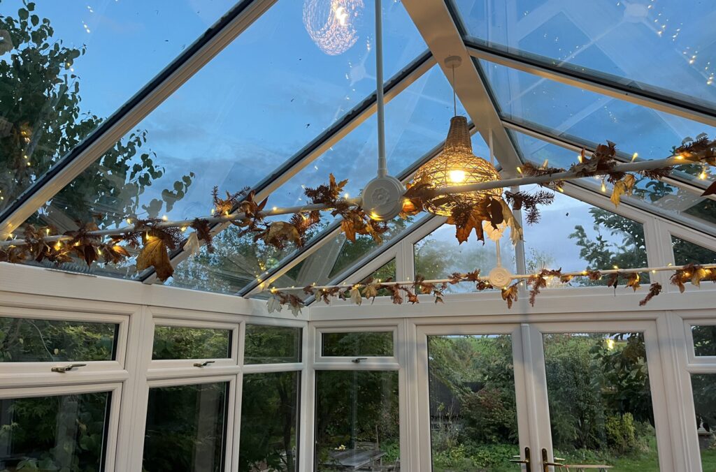 slow living - burnt orange dried firr and mahonia garlands and fairy lights adorning the conservatory in the evening.